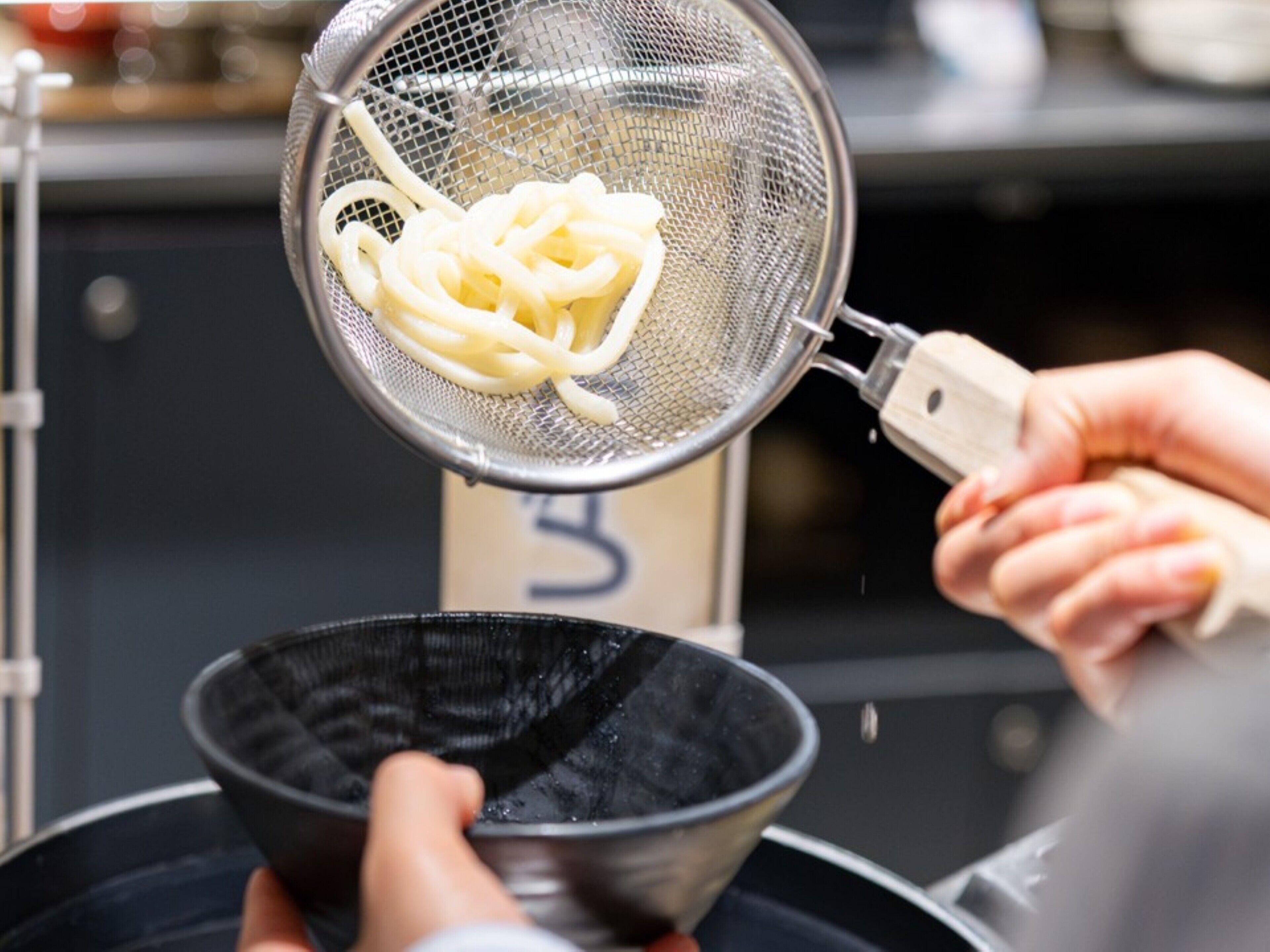 A person using a strainer to drain noodles into a bowl.
