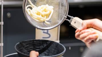 A person using a strainer to drain noodles into a bowl.