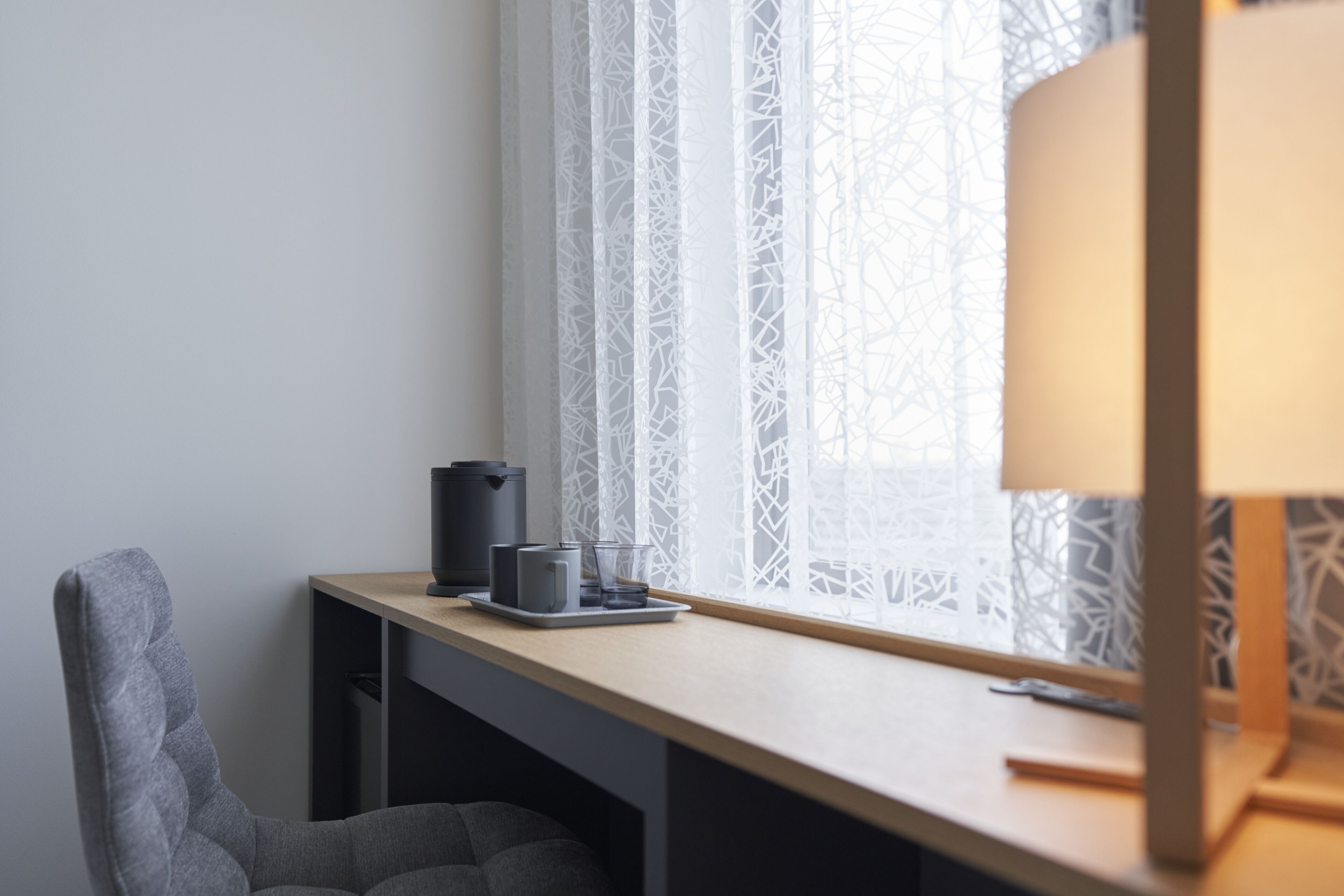 A minimalist workspace with a desk, chair, and a window with patterned curtains.
