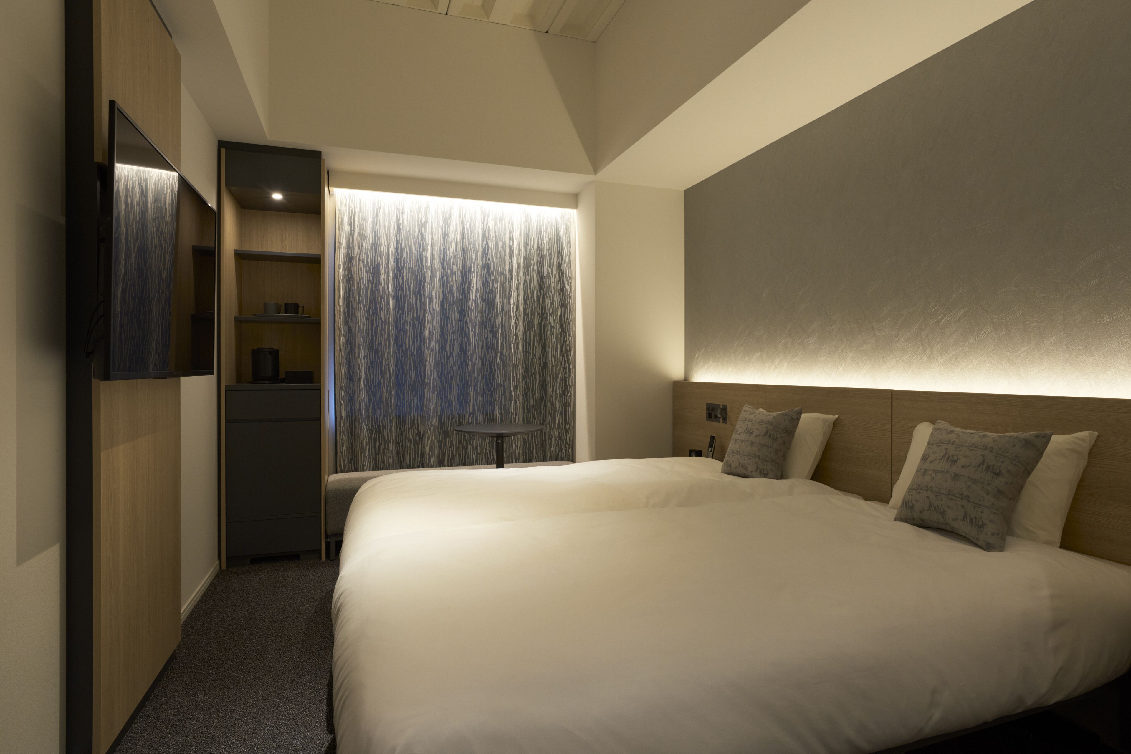 A modern hotel room with a large bed, a wardrobe, a desk, and a view of a forest through a window.