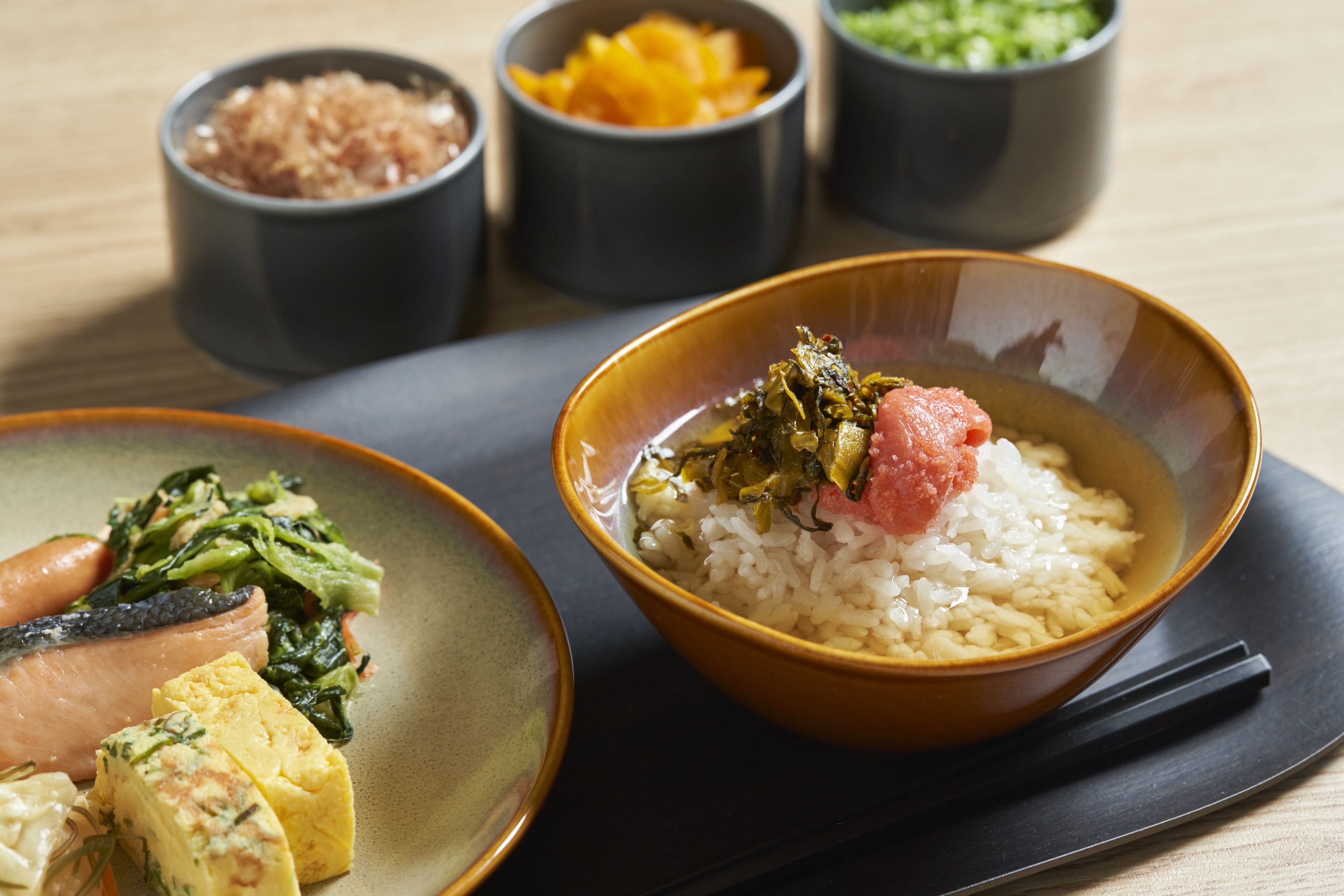 A meal with rice, fish, and vegetables on a plate, accompanied by small bowls of condiments.