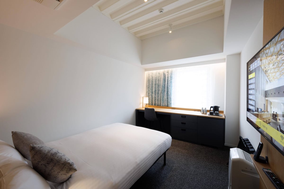 Une chambre d’hôtel moderne avec un lit simple, un bureau et une grande fenêtre.