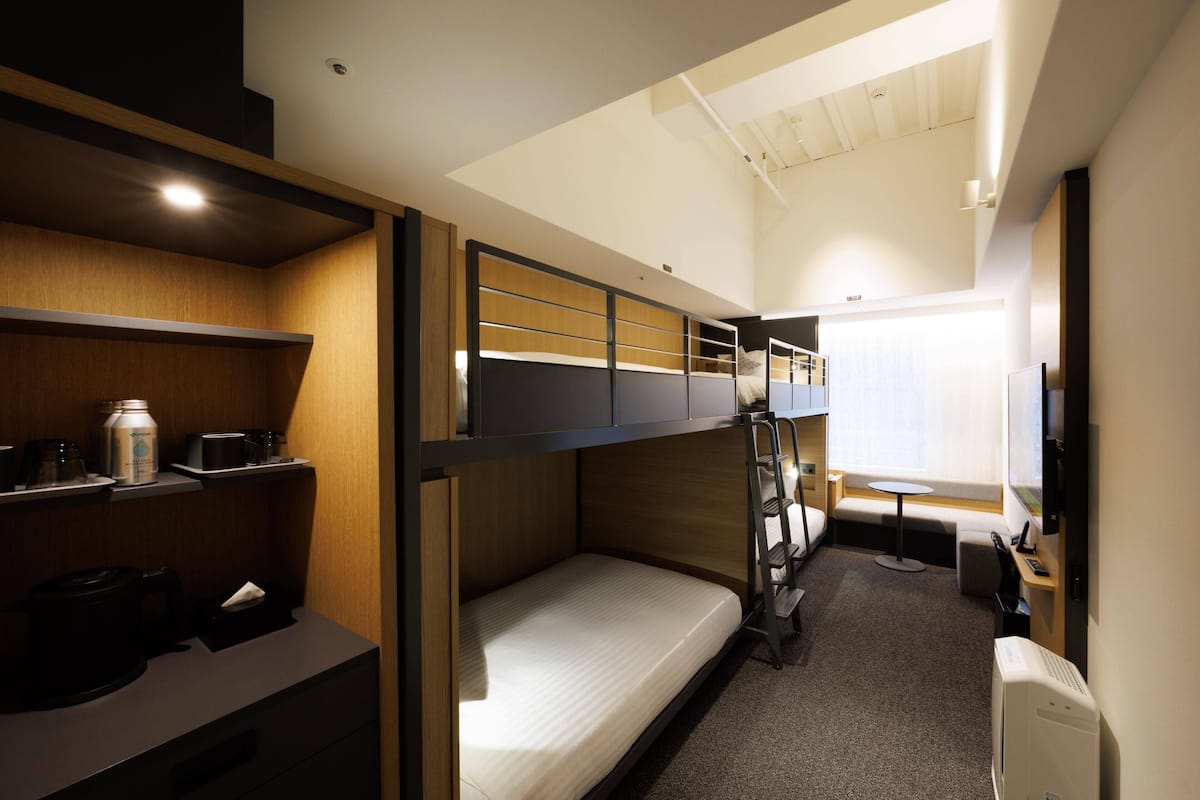 Une chambre avec un lit superposé, un bureau, une petite table et une fenêtre.