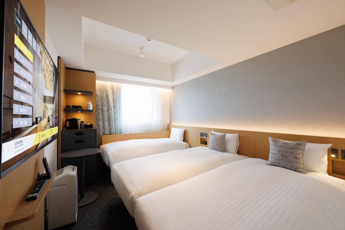 Une chambre d’hôtel avec deux lits, un bureau avec un ordinateur, une petite table et une fenêtre avec des rideaux.