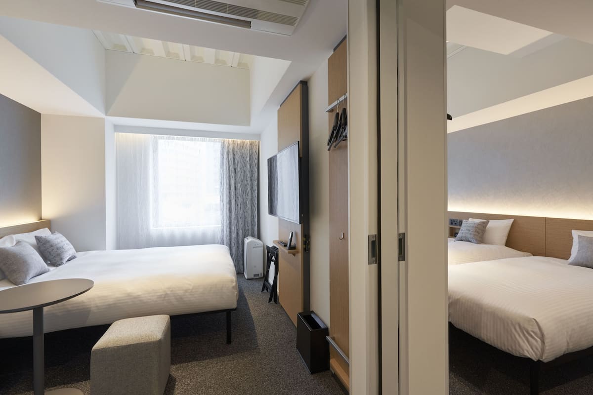 Une chambre d’hôtel avec deux lits, un bureau, une chaise, une télévision et une fenêtre avec des rideaux.