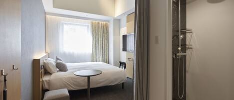 A modern hotel room with a bed, a small round table, a shower area, and a television.