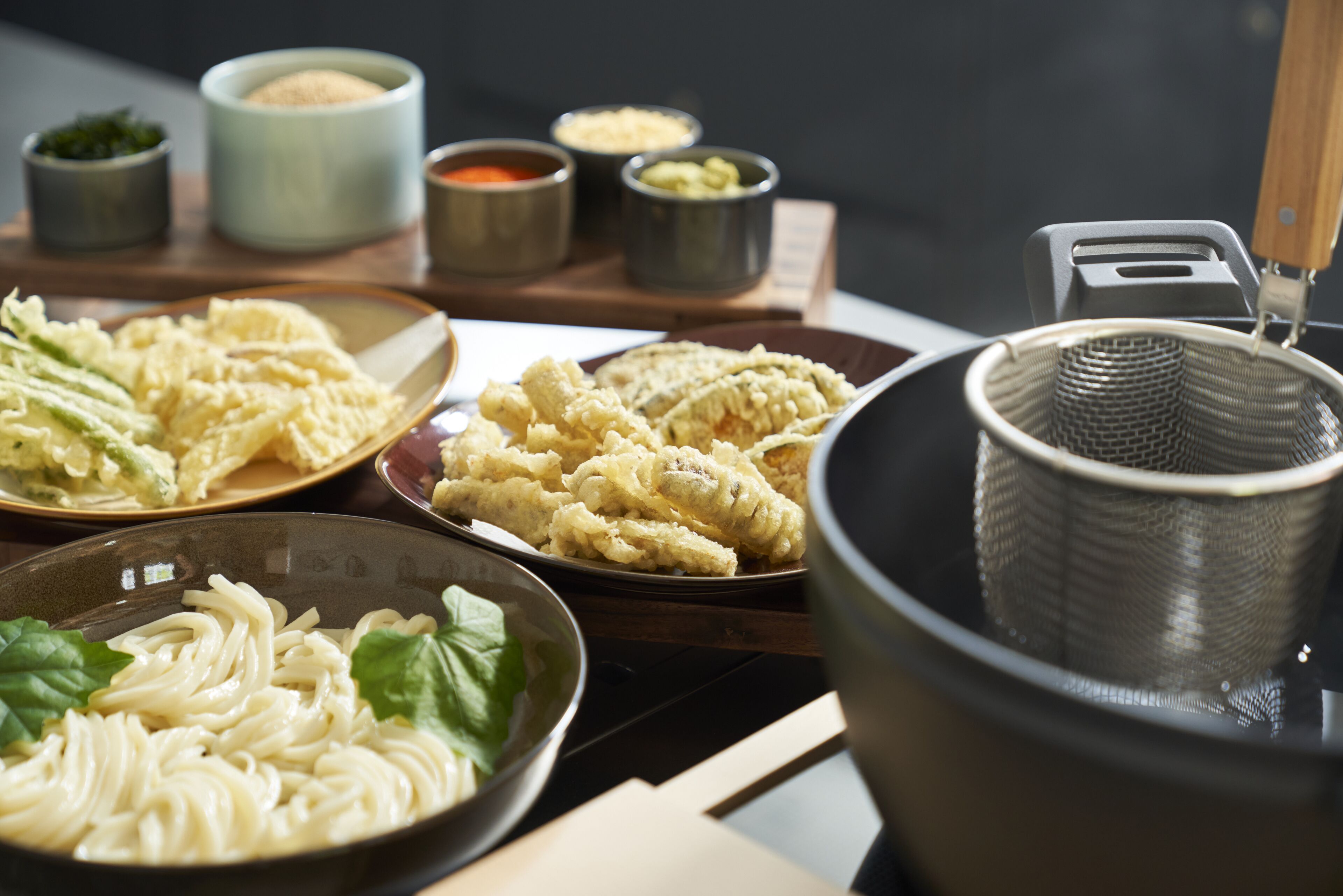 Een tafel met verschillende gerechten, waaronder noedels, tempura en kleine schaaltjes met sauzen.