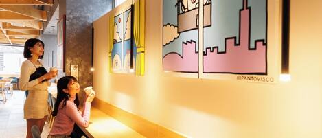 A cafe with wooden tables and chairs, a large window, and colorful wall art.