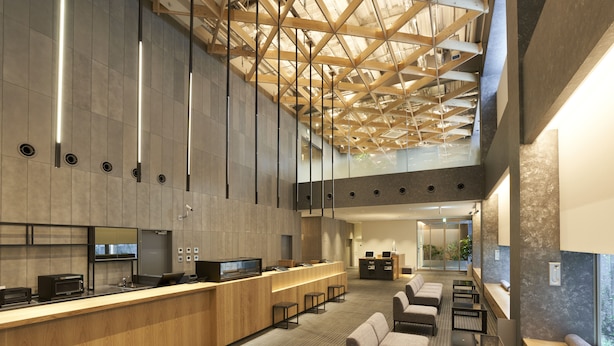 Un hall d’hôtel moderne doté d’un comptoir d’accueil, d’un espace salon et d’un plafond haut avec des poutres apparentes.