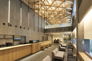 Un hall d’hôtel moderne doté d’un comptoir d’accueil, d’un espace salon et d’un plafond haut avec des poutres apparentes.