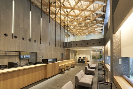 A modern hotel lobby with a reception desk, seating area, and a high ceiling with exposed beams.