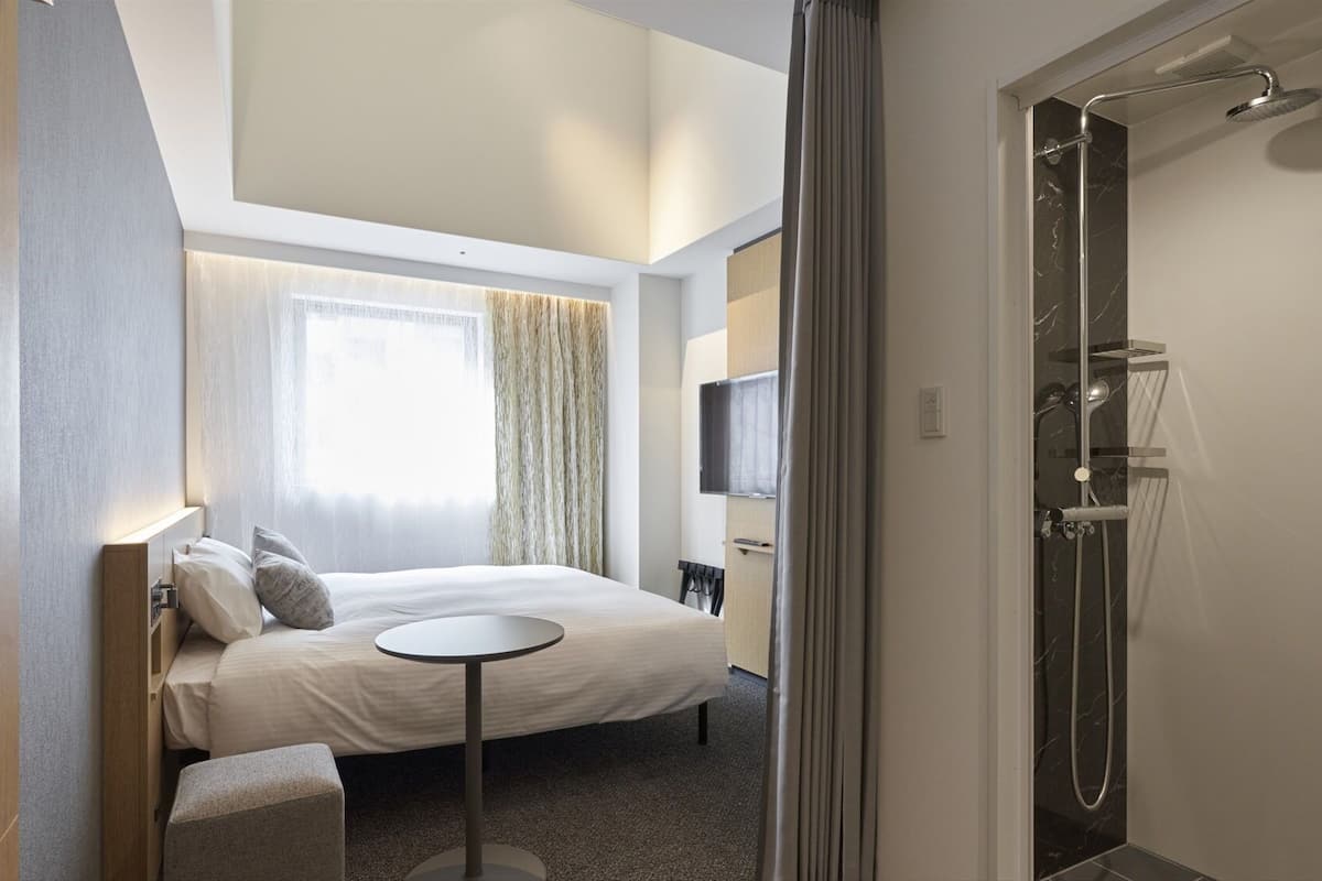 Une chambre d’hôtel avec un lit, une petite table, une télévision et une douche.
