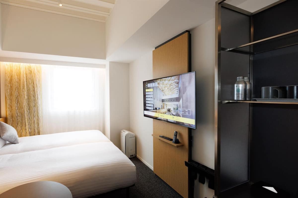 Une chambre d’hôtel avec un lit, un téléviseur fixé au mur, une armoire et une étagère avec quelques objets.
