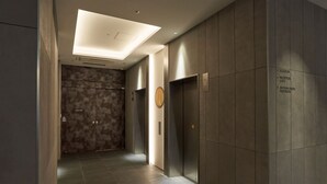 Un espace moderne pour les ascenseurs, avec un panneau indiquant « RESERVÉ AU PERSONNEL », un panneau de commande d’ascenseur et des panneaux de signalisation indiquant « ASCENSEUR », « RÉCEPTION » et « TOILETTES (SALLE DE DANSE) ».