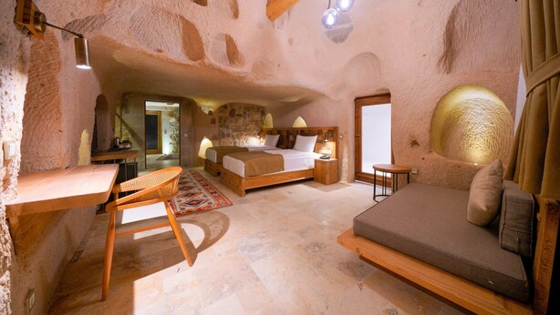 A rustic bedroom with a large bed, a wooden desk, and a sofa. - Kappadoks Cave Hotel (Nevsehir)