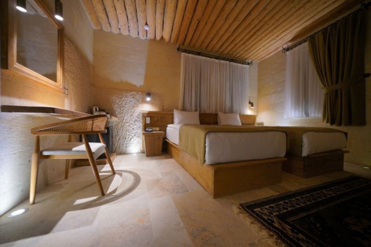 A cozy bedroom with a wooden ceiling, a bed with white linens, a small desk, and a chair.