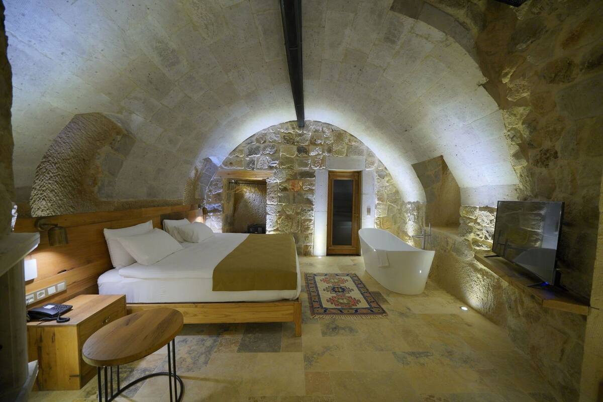 A stone-walled bedroom with a bed, a bathtub, and a TV.