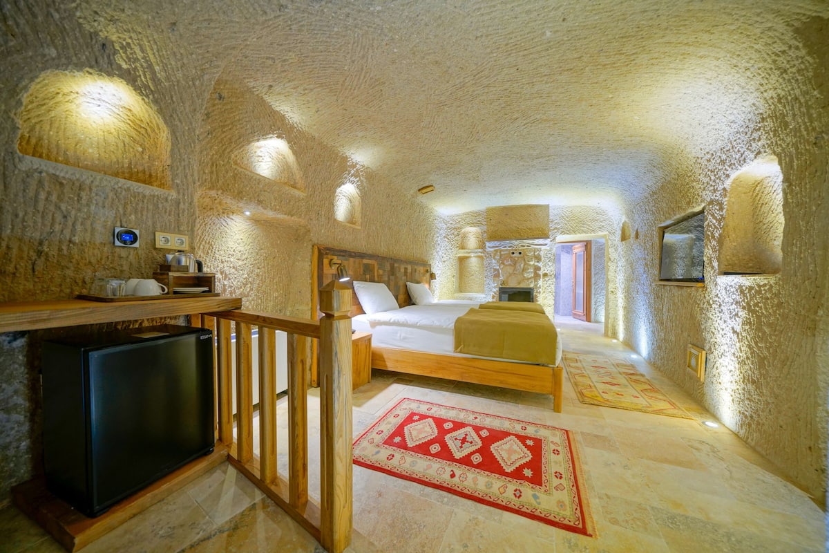 A cozy, cave-like bedroom with a bed, wooden furniture, and a small TV.