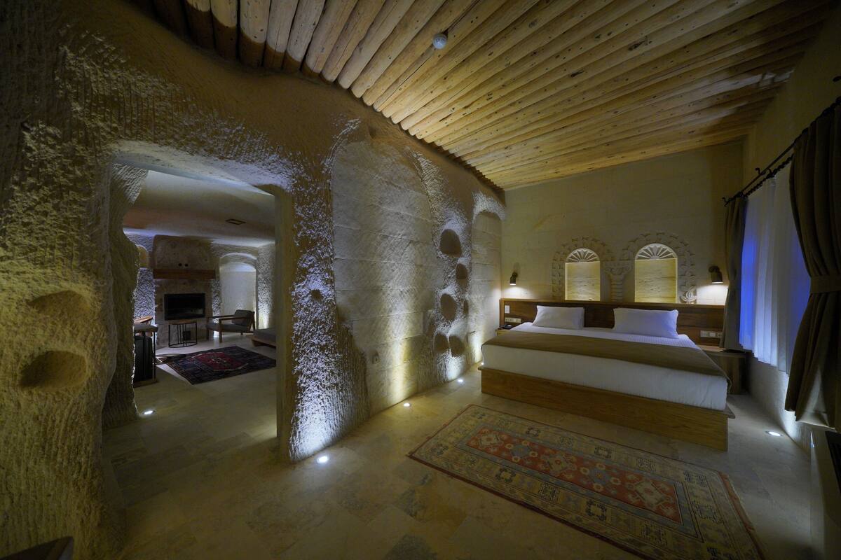 A bedroom with a stone wall, a wooden ceiling, a large bed, and a TV in the corner.