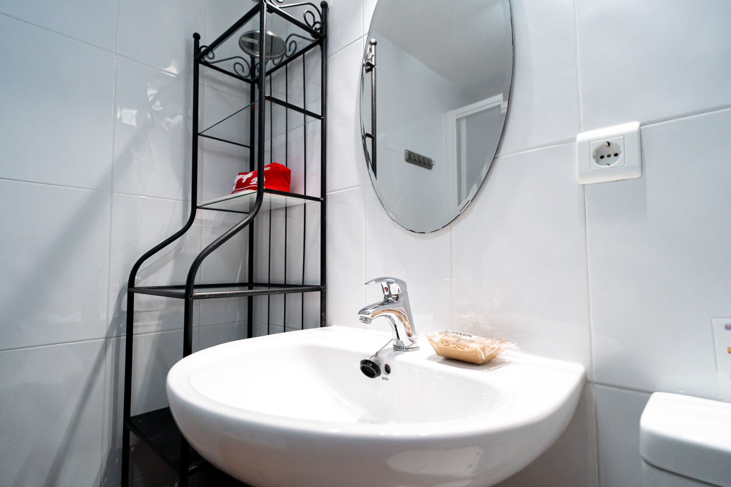 A bathroom with a white sink, a mirror, and a metal shelf with a red object.