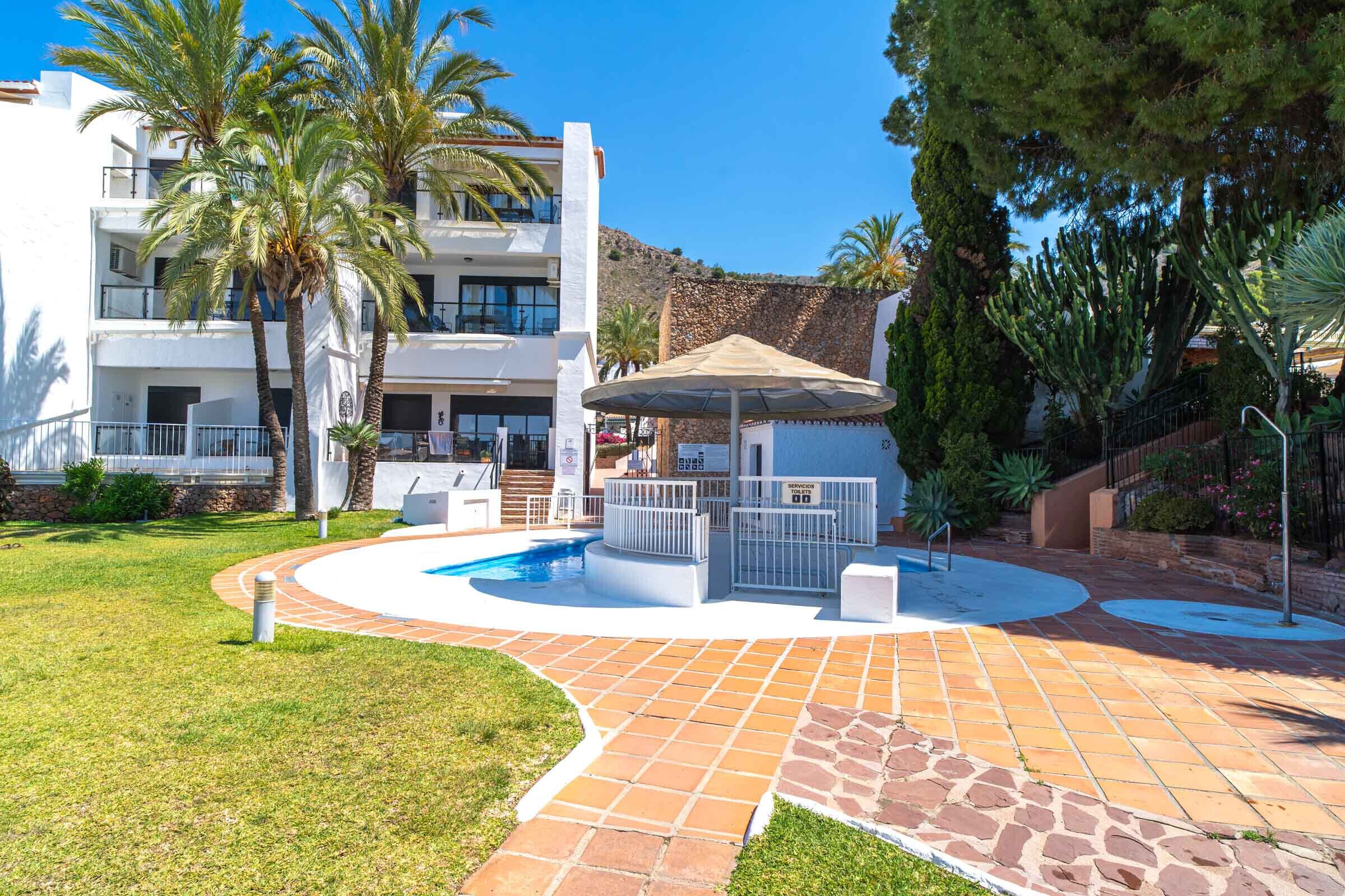 A pool area with a circular design, palm trees, and a white building with balconies.