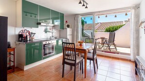 Una cocina compacta con gabinetes verdes, una mesa de comedor con sillas y vistas a un tejado con tejas a través de una puerta corrediza de vidrio.
