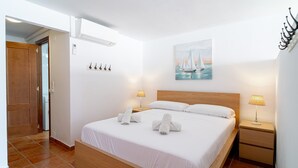 Una habitación de hotel con una cama de madera, ropa blanca de cama, un cuadro de un velero, dos lámparas de noche y una mesita de noche de madera.