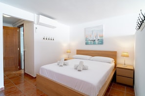 A hotel room with a wooden bed, white linens, a painting of a sailboat, two bedside lamps, and a wooden nightstand.