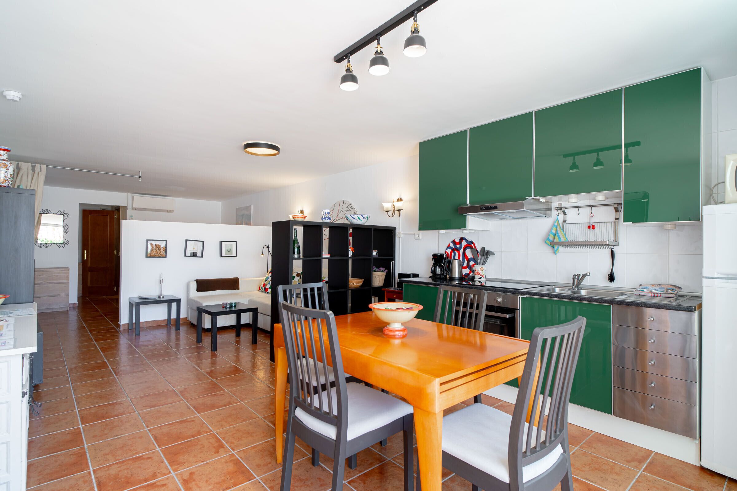A modern kitchen with green cabinets, a dining table with chairs, and a visible kitchen island.