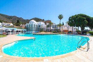 A swimming pool with a wooden deck, a palm tree, and a building with a dome in the background.