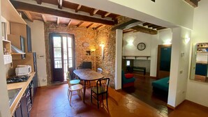 Une cuisine équipée d’une cuisinière, d’un four à micro-ondes et de placards, un coin repas avec une table et des chaises, et un mur en pierre orné d’une horloge et d’un panneau indiquant la présence d’une connexion Wi-Fi.