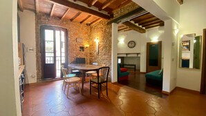Un intérieur rustique avec un mur en pierre, des poutres en bois, un coin repas avec des chaises, un canapé et une cheminée.