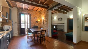 Un intérieur rustique avec un mur en pierre, des poutres en bois, un coin repas avec des chaises, une cuisine équipée d’une cuisinière et une cheminée.