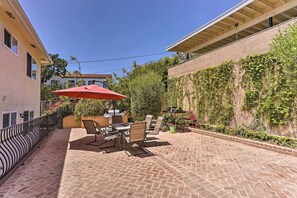 Eine Terrasse im Freien mit Backsteinboden, einem Tisch mit Stühlen und einem roten Sonnenschirm.
