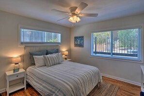 Ein Schlafzimmer mit einem Bett, zwei Nachttischen mit Lampen, einem Deckenventilator und zwei Fenstern mit Jalousien.