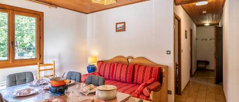 A dining area with a wooden table set for a meal, a sofa with red cushions, and a wooden ceiling.