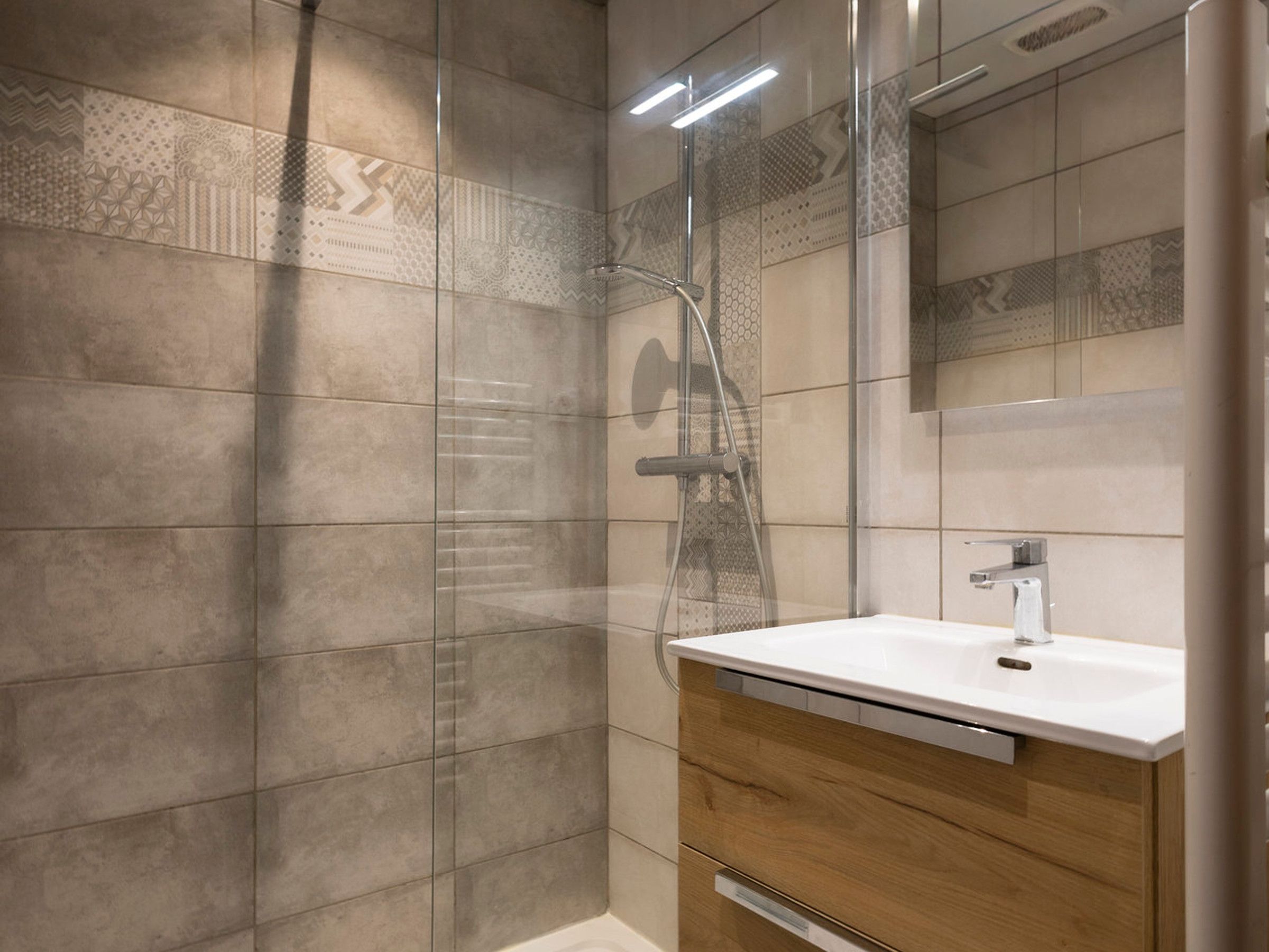 Een moderne badkamer met een douchecabine van glas, een witte wastafel en een houten opbergmeubel.