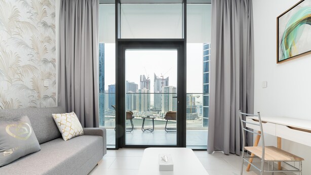 A modern living room with a grey sofa, a white coffee table, and a view of a cityscape through large windows. - GLOBALSTAY. New Marquise Square Building in Business Bay (Dubai)