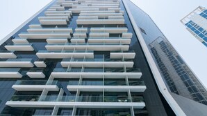 A modern high-rise building with a distinctive facade featuring a series of horizontal white panels and reflective glass windows. - GLOBALSTAY. New Marquise Square Building in Business Bay (Dubai)