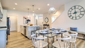 A modern kitchen with white cabinetry, a dining area with a glass table, and a large wall clock. - Family-Friendly Home: 4 Mi to Bethany Beach! (Millville)