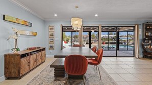 A dining area with a large table, red chairs, a wooden cabinet, and a view of a swimming pool and outdoor area. - Gulf Access, Minutes to the River, Kayaks & Dog Friendly - Aqua Escape - Roelens Vacations (Cape Coral)
