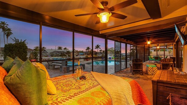 A spacious room with a large bed, a ceiling fan, and a view of a swimming pool and palm trees. - Gulf Access, Minutes to the River, Kayaks & Dog Friendly - Aqua Escape - Roelens Vacations (Cape Coral)