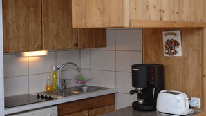 Keittiössä on puukehikoiset kaapit, pesuallas, liesi, kahvinkeitin ja leivänpaahdin.
