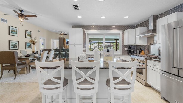 A modern kitchen with white cabinetry, a stainless steel refrigerator, and a dining area with white chairs and a table. - Boat lift -Direct Gulf Access, Great Spaces inside & out!  - Villa Ocean Pearl - Roelens Vacations (Cape Coral)