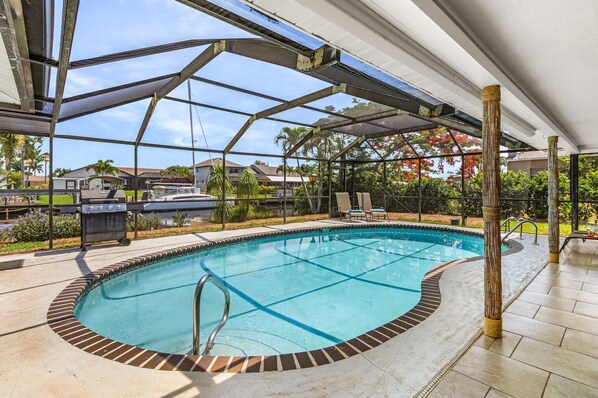A swimming pool with a glass bottom, surrounded by a covered patio area with a metal roof structure.