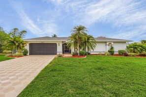 A single-story house with a dark garage door, a well-maintained lawn, and a palm tree.