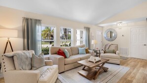 Ein großzügiges Wohnzimmer mit einem beigen Sofa, einem Holztisch und Blick ins Freie durch große Fenster.