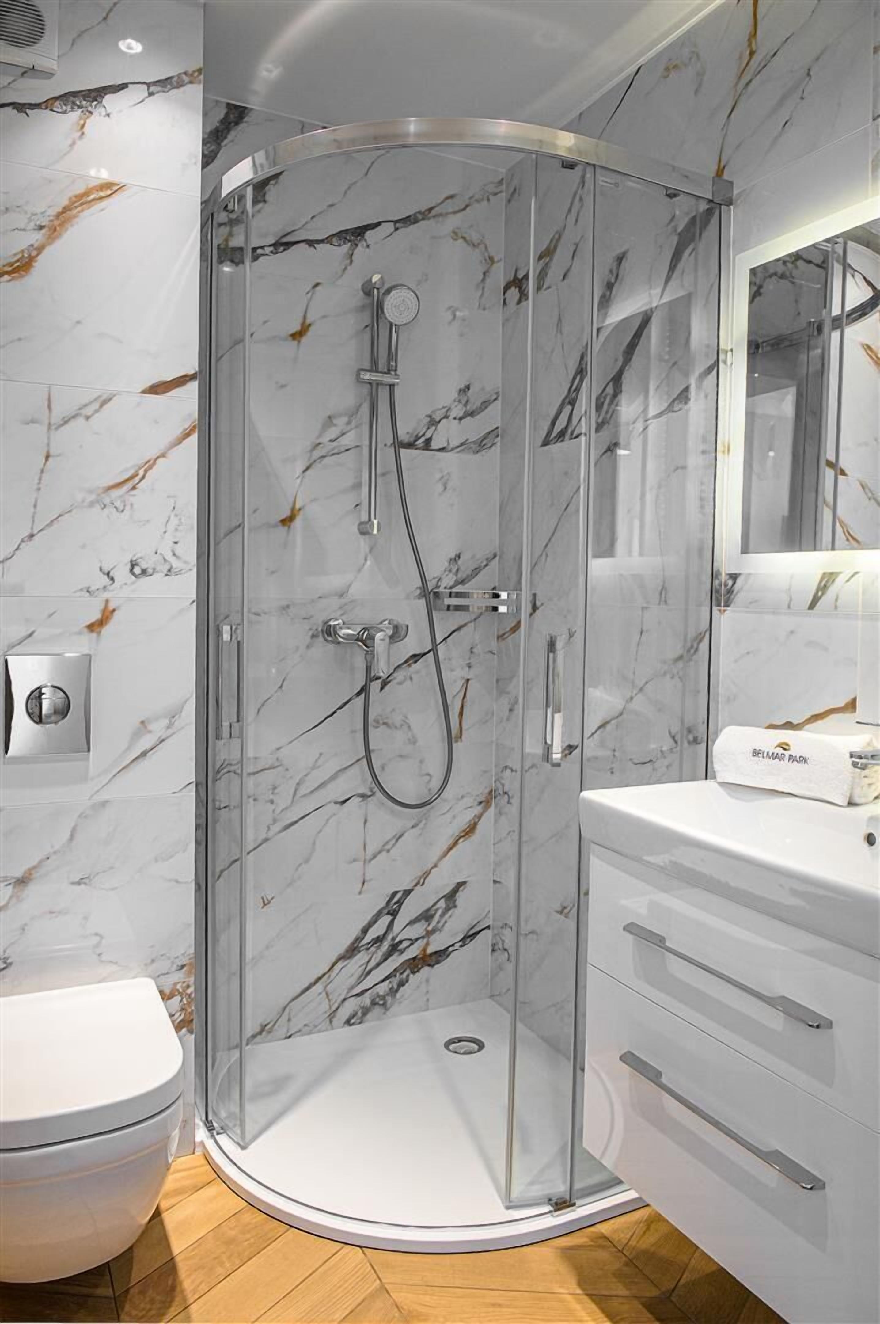 Une salle de bain moderne avec une douche à parois de verre, des murs en marbre et un meuble-lavabo blanc.