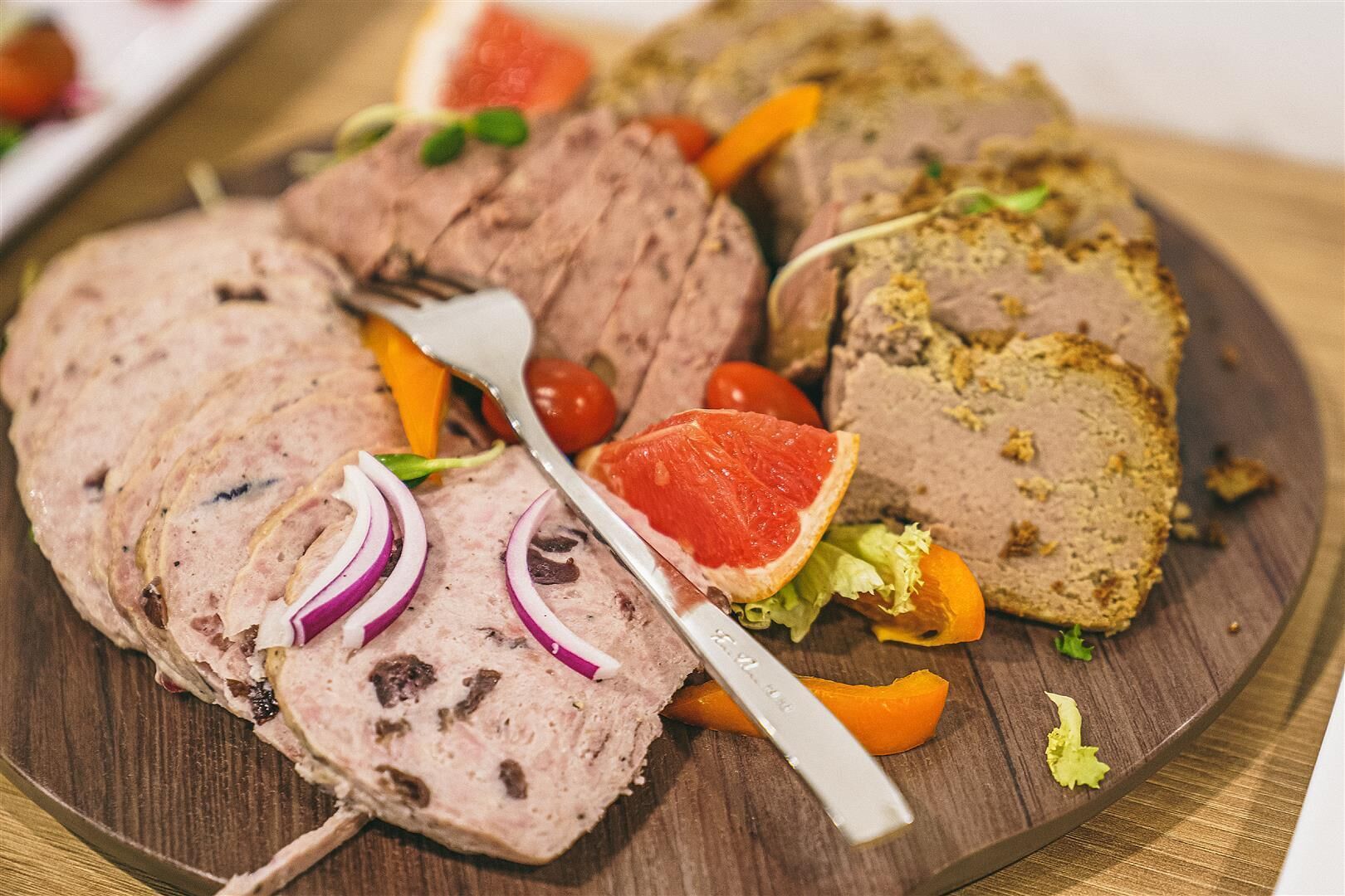 Une planche en bois sur laquelle sont disposées des tranches de pain de viande, garnies d’oignons rouges en rondelles, de tomates cerises et d’un demi-pamplemousse.