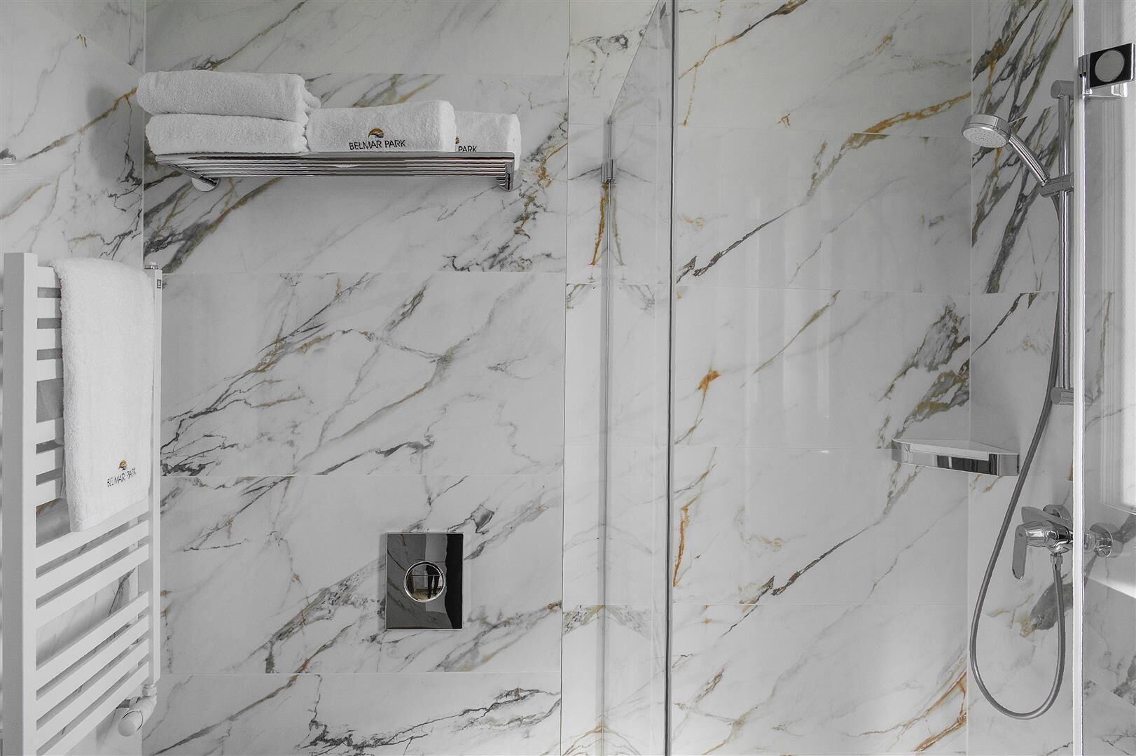 A bathroom with marble walls, a towel rack with towels, a shower area, and a control panel.